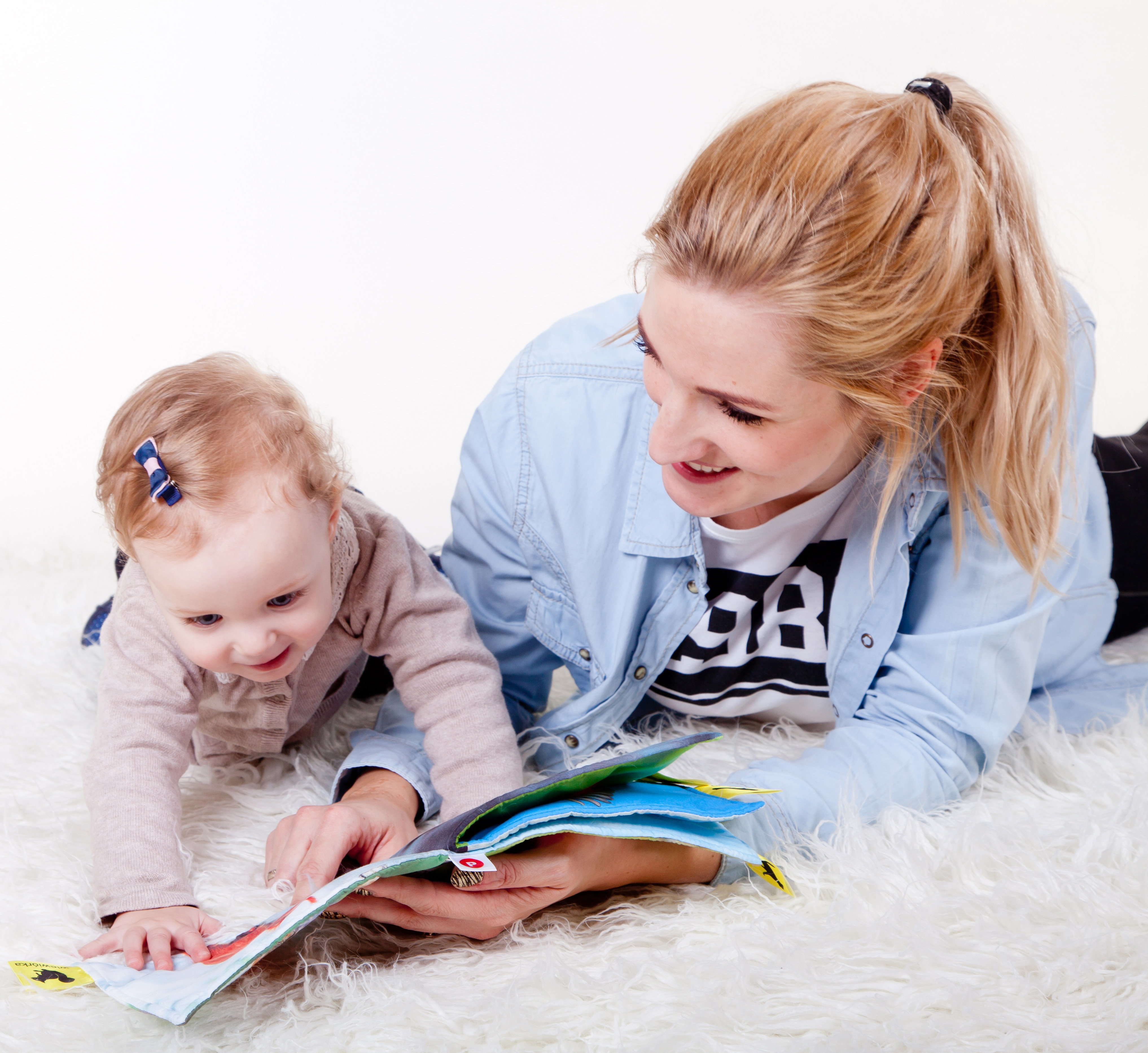 Image of mother and baby girl reading on a white carpet.