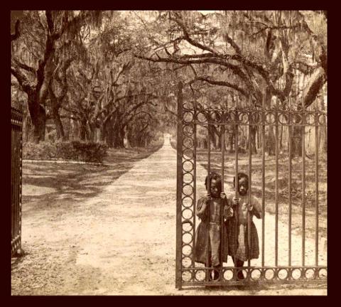 Two young African American girls standing behind the bars of a gate.