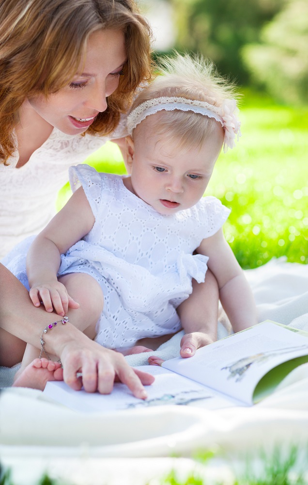 small baby reading outdoors with mother