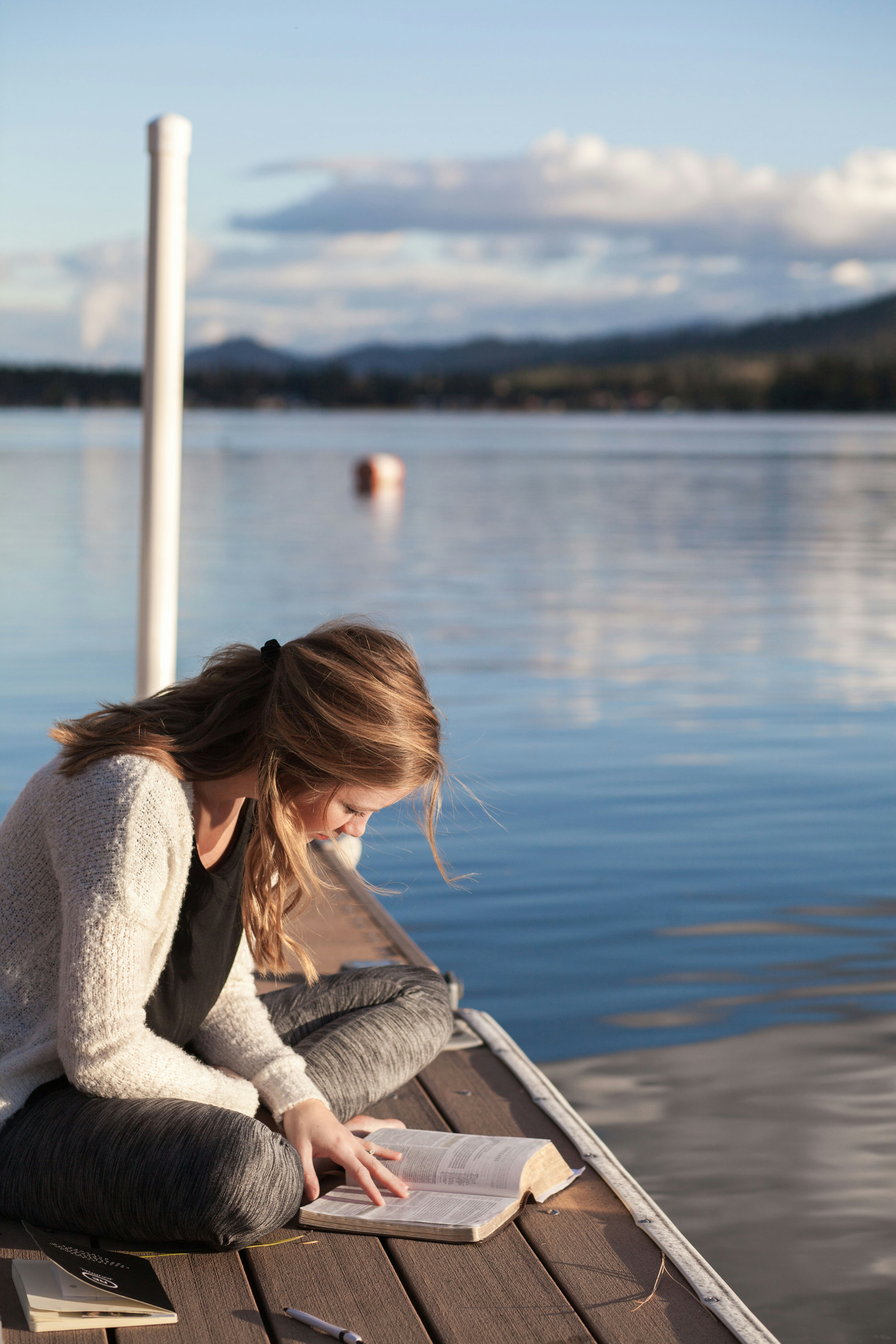 A woman reads a book on a dock.