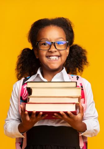 Young, smiling, African-American girl holding a stack of books.
