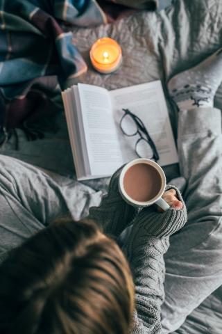 Woman reading a book and holding a mug with cocoa or coffee inside.