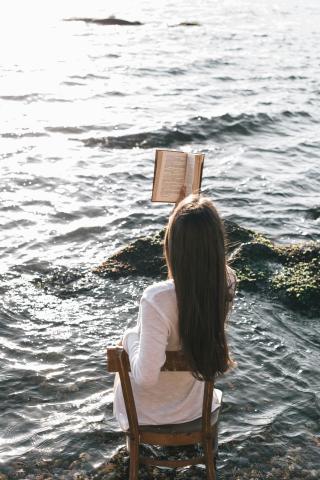 A woman reads a book on a chair in the ocean.