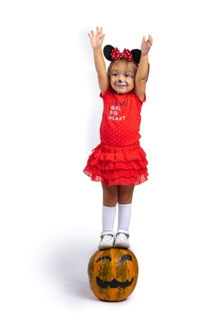 Cute little girl dressed in Minnie Mouse costume and standing on a pumpkin.