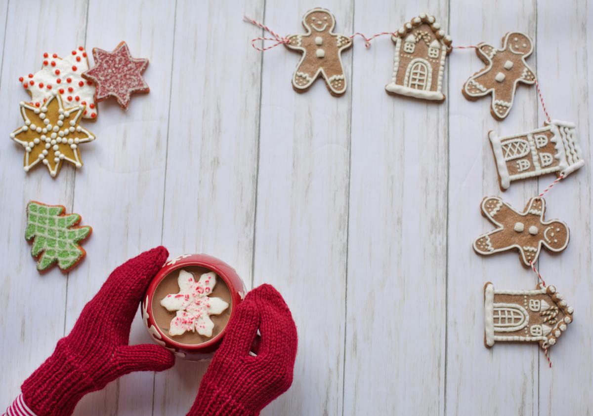 Mittens holding cocoa surrounded by gingerbread cookies