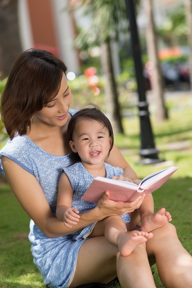 Asian Mom with baby girl reading in the park.